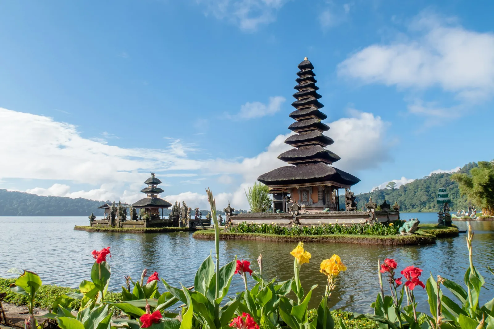 Los santuarios escalonados de Pura Ulun Danu Bratan se levantan a orillas de un lago de montaña en Bali, detrás de flores rojas y amarillas.