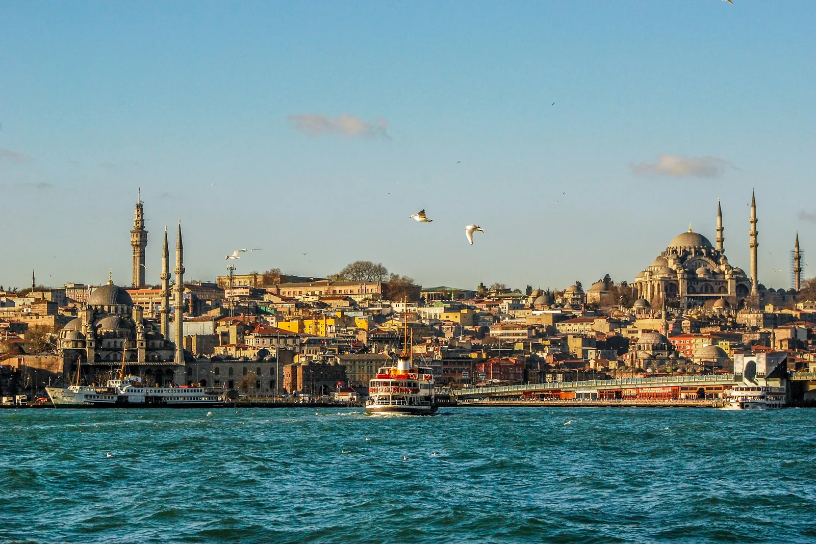 A white ferry crosses the Bosphorus in front of Eminönü, with mosque domes and minarets on the skyline.