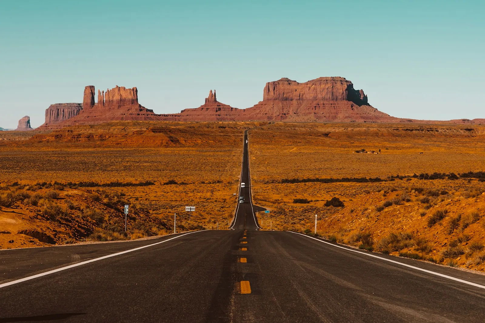 A straight highway runs through orange desert towards the sandstone buttes of Monument Valley.